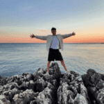 A Man Standing On A Rock In Front Of The Sea And Spreading His Arms Appart